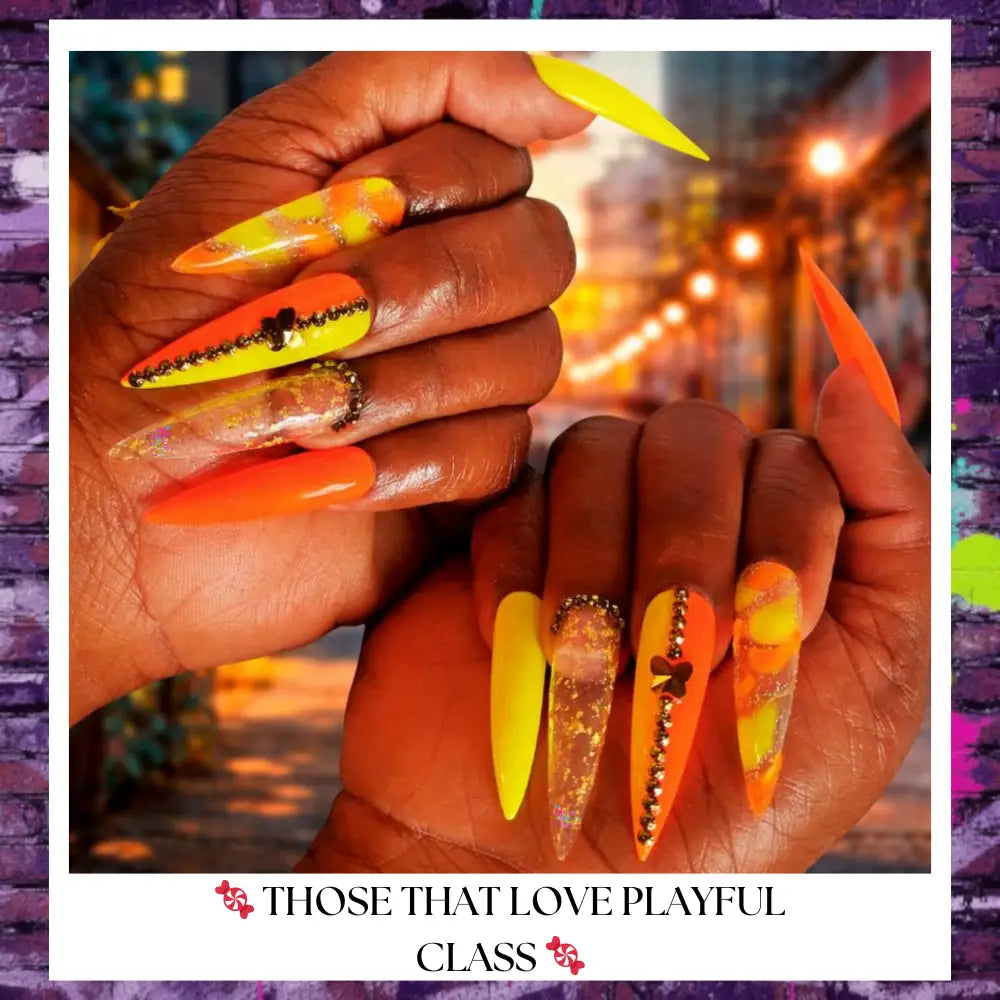Close-up of neon orange and electric yellow stiletto press on nails with jelly candy accents, gold rhinestones, and glossy finish on hands against a vibrant yellow background.