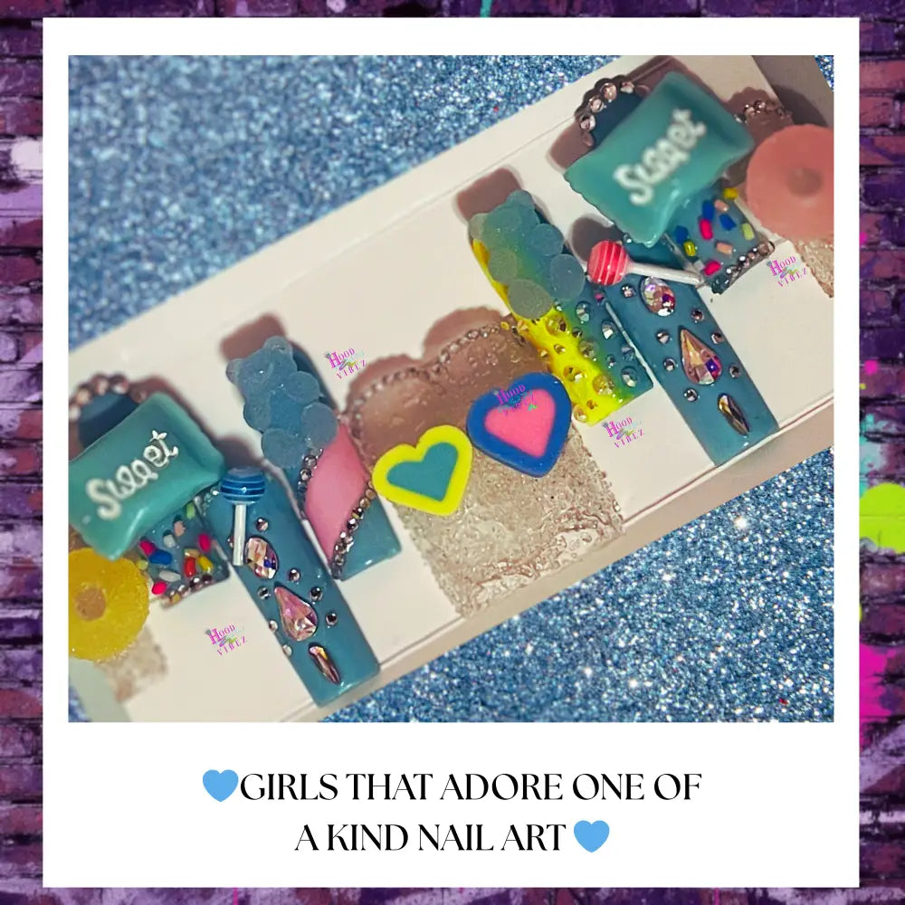 “Aqua candy-themed press on nails with sprinkles, rhinestones, and 3D charms arranged on a white card with a sparkly blue background.”