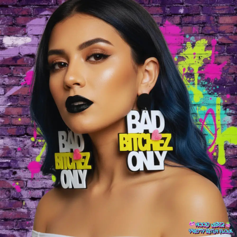Woman wearing 'BAD BITCHEZ ONLY' earrings with a colorful graffiti-style brick wall background