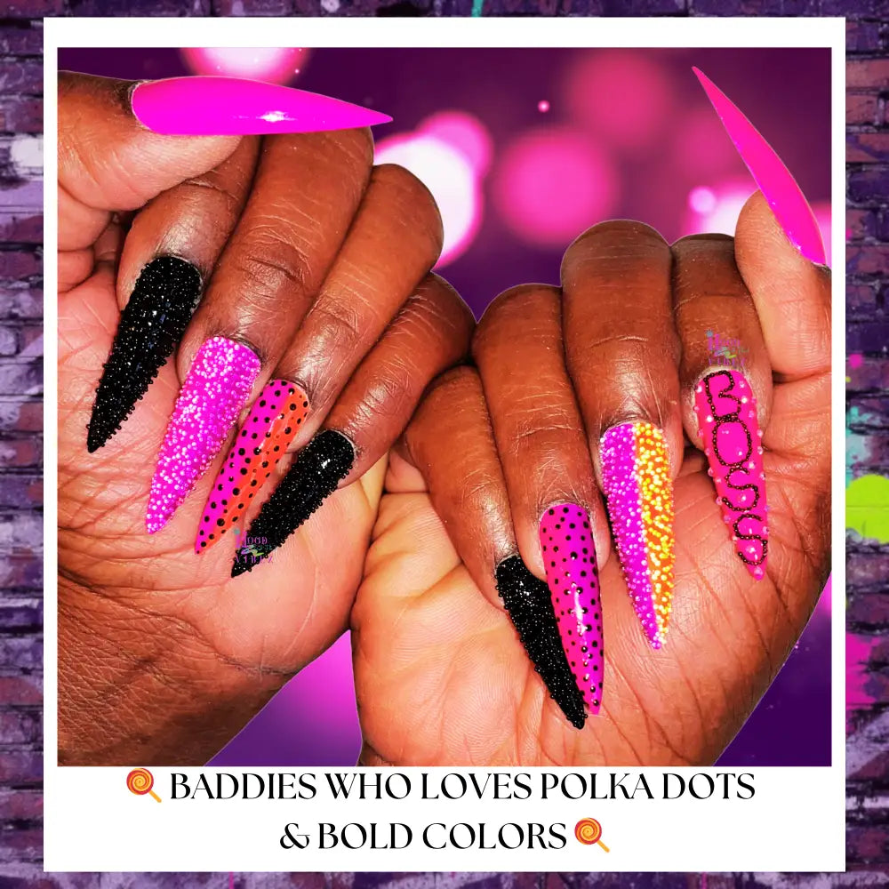 Hand model wearing Candy Coated press-on nails featuring hot pink, black, and neon designs with rhinestone texture, polka dot accents, and glossy stiletto shapes on a vibrant pink bokeh background.