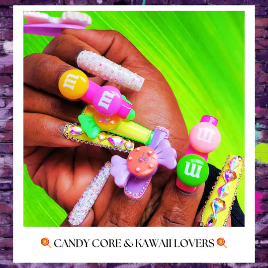 Candy-core press on nails with vibrant pink, green, and yellow tones featuring 3D candy charms, rhinestone embellishments, and glossy long nail designs displayed on hands against a bold green background.
