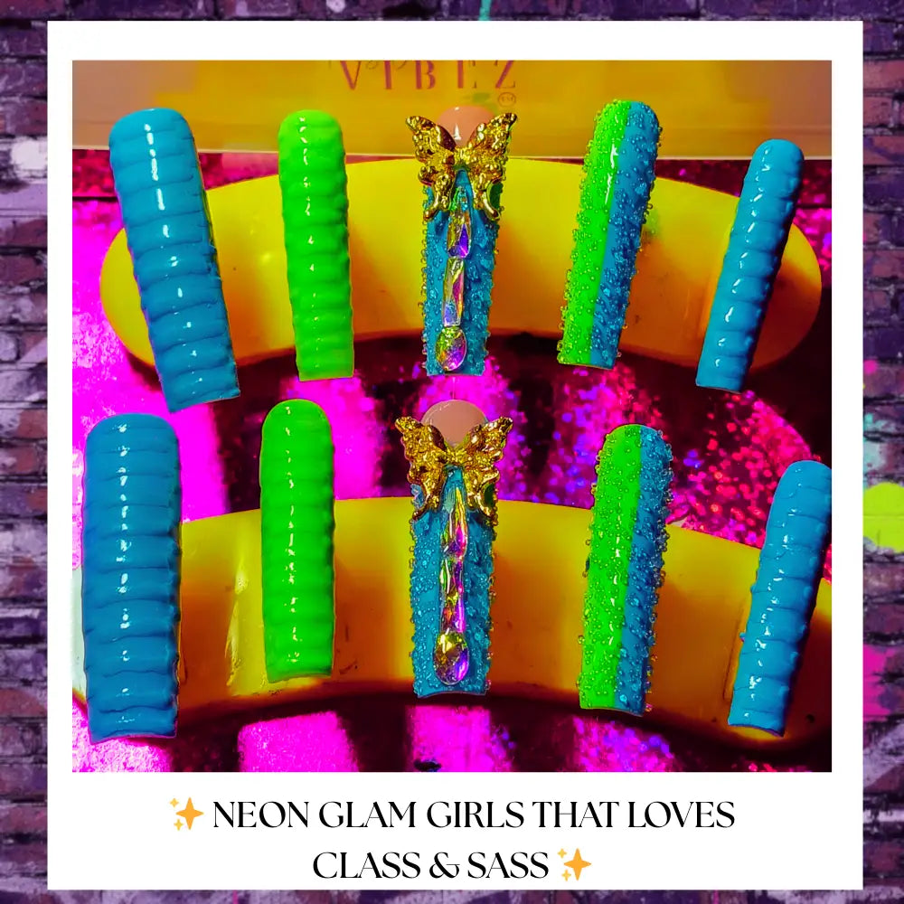 “Bright neon press on nails in turquoise, lime green, and glitter blue with gold butterfly charms and gemstone accents displayed against a pink-purple glitter background on a yellow nail stand.”