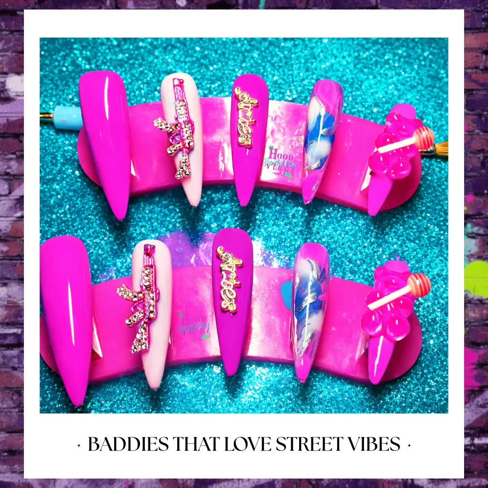 Hot pink street glam press on nails with rhinestone gun charms, glossy finish, and bold Barbie core design displayed on glitter background.