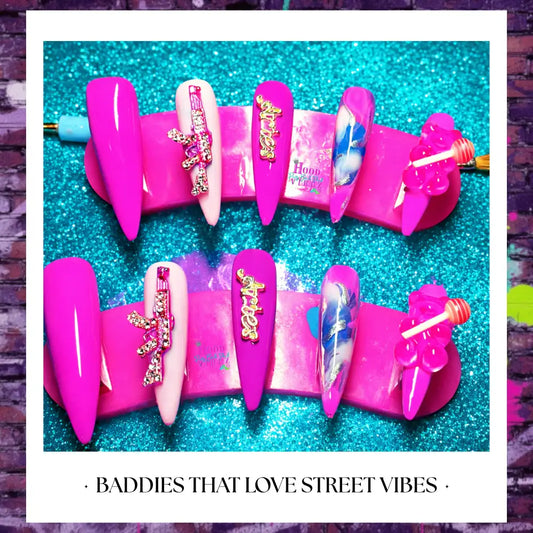 Hot pink street glam press on nails with rhinestone gun charms, glossy finish, and bold Barbie core design displayed on glitter background.