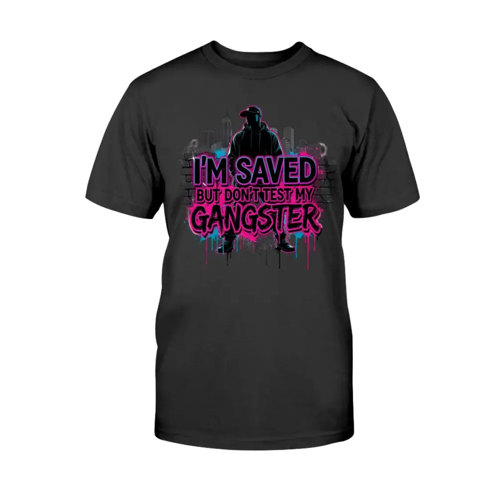 I’m Saved But Don’t Test My Gangster graphic t-shirt featuring bold pink graffiti lettering, urban skyline background, and streetwear silhouette design on black tee.