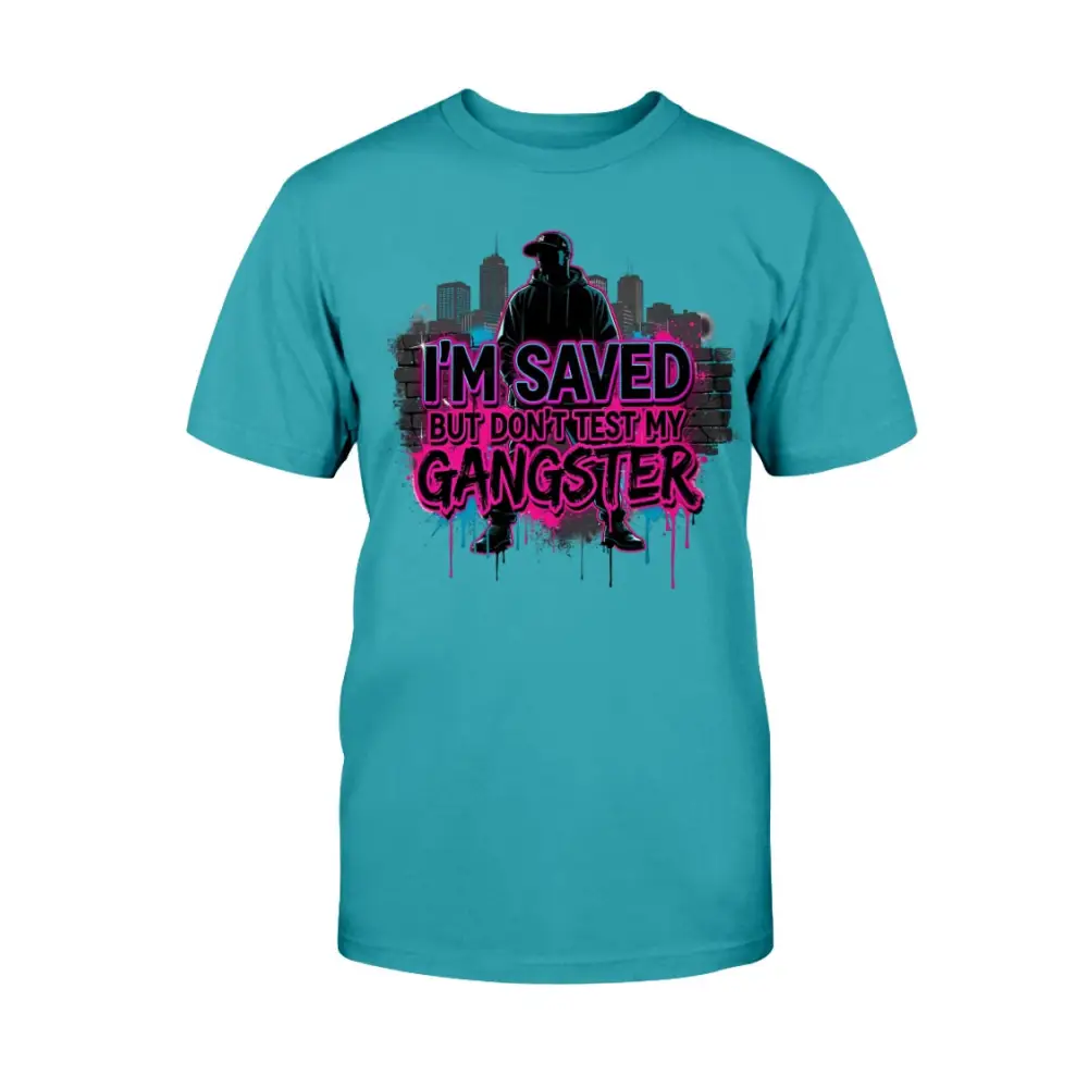 I’m Saved But Don’t Test My Gangster graphic t-shirt featuring bold pink graffiti lettering, urban skyline background, and streetwear silhouette design on teal tee.