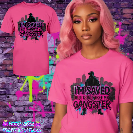 MODEL WEARING I’m Saved But Don’t Test My Gangster graphic t-shirt featuring bold pink graffiti lettering, urban skyline background, and streetwear silhouette design on hot pink tee.
