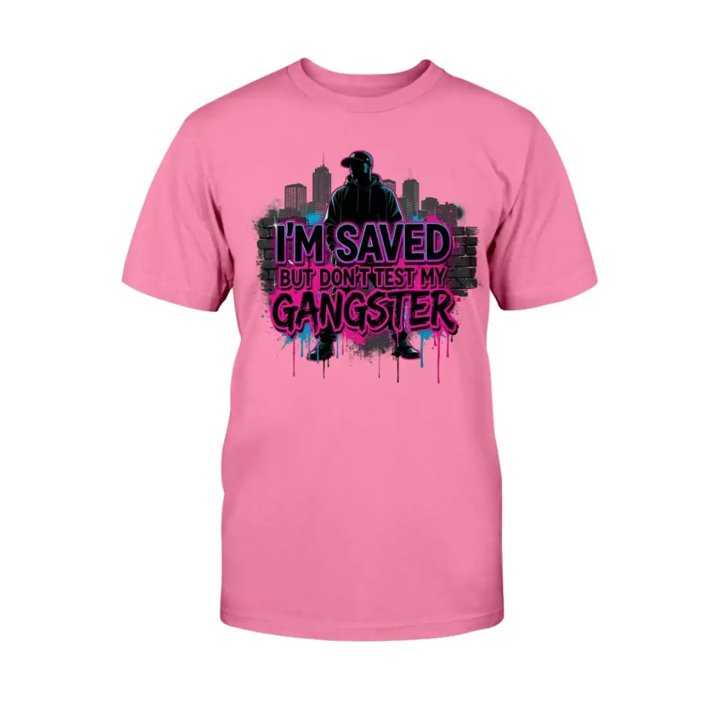 I’m Saved But Don’t Test My Gangster graphic t-shirt featuring bold pink graffiti lettering, urban skyline background, and streetwear silhouette design on pink tee.