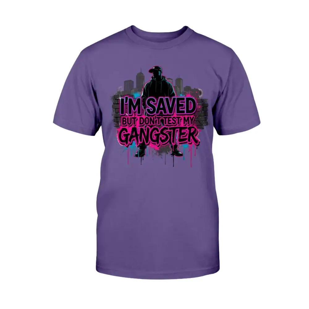 I’m Saved But Don’t Test My Gangster graphic t-shirt featuring bold pink graffiti lettering, urban skyline background, and streetwear silhouette design on purple tee.