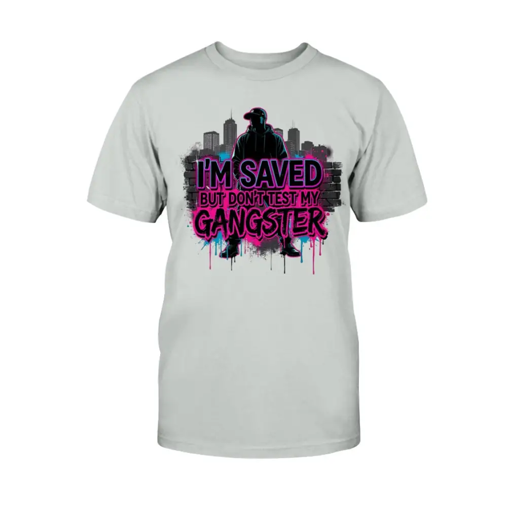 I’m Saved But Don’t Test My Gangster graphic t-shirt featuring bold pink graffiti lettering, urban skyline background, and streetwear silhouette design on ash grey tee.