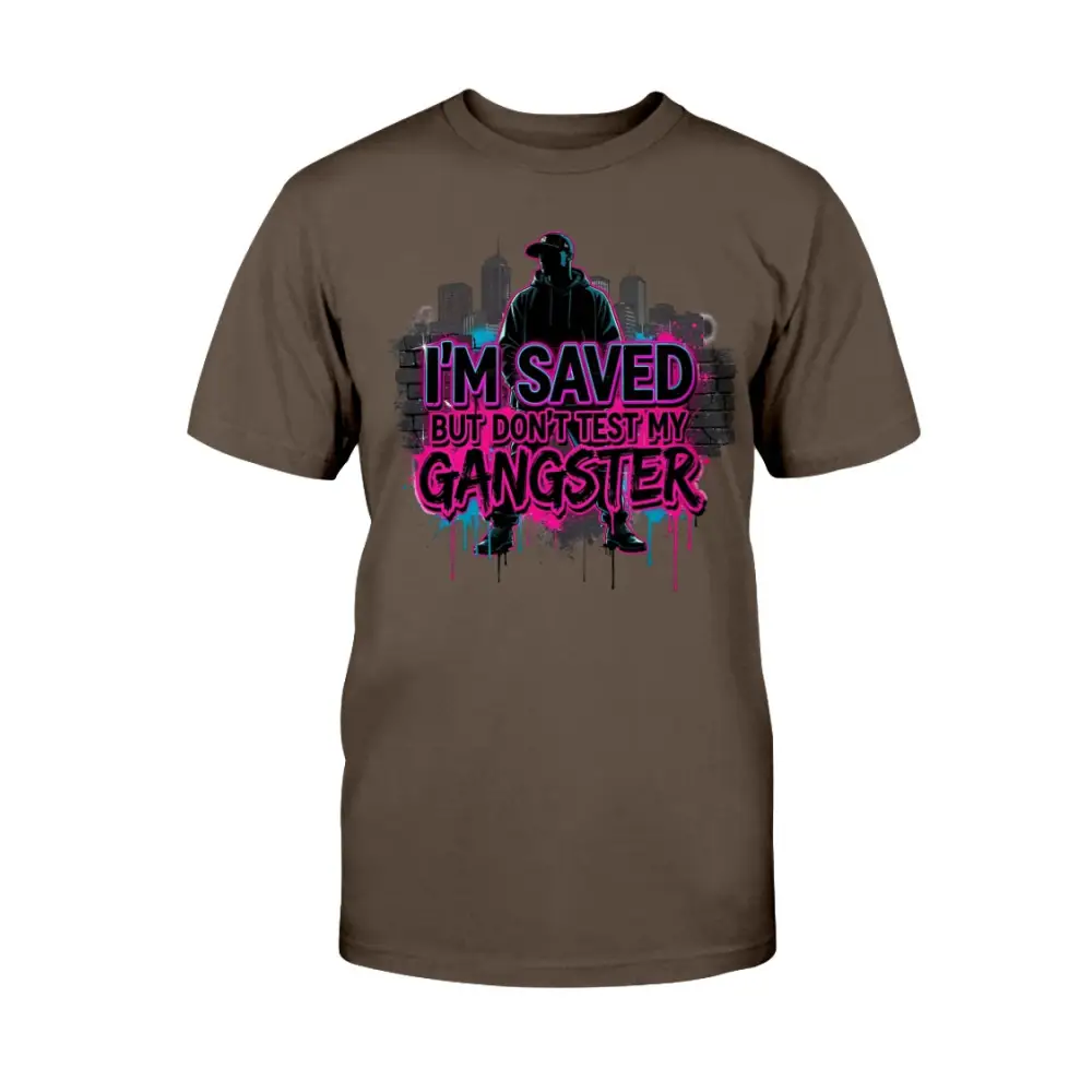 I’m Saved But Don’t Test My Gangster graphic t-shirt featuring bold pink graffiti lettering, urban skyline background, and streetwear silhouette design on brown tee.