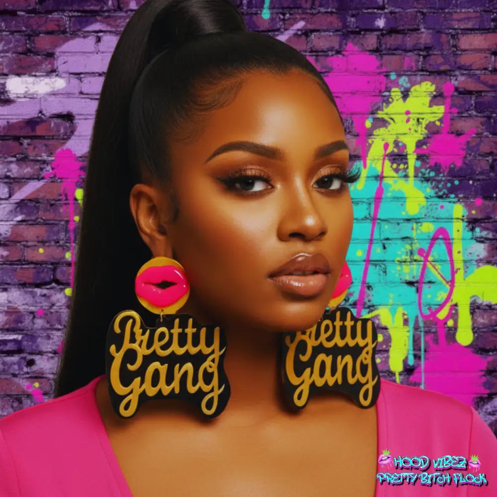Pretty Gang statement earrings featuring gold script lettering on black acrylic with pink lip accents and round gold studs on a white background.