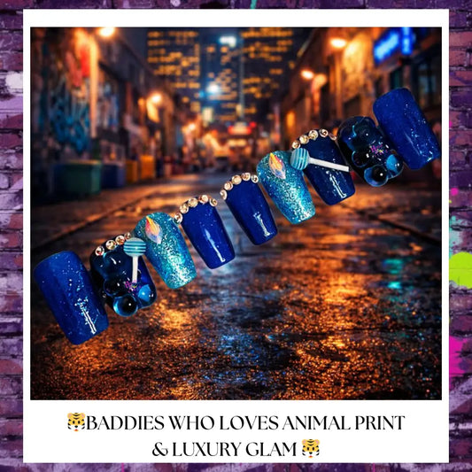 Close-up of Berry Blue Drip press-on nails featuring deep blue and teal shades with glitter accents, small rhinestones along the cuticle, and candy-inspired charm details on a textured urban-style background.
