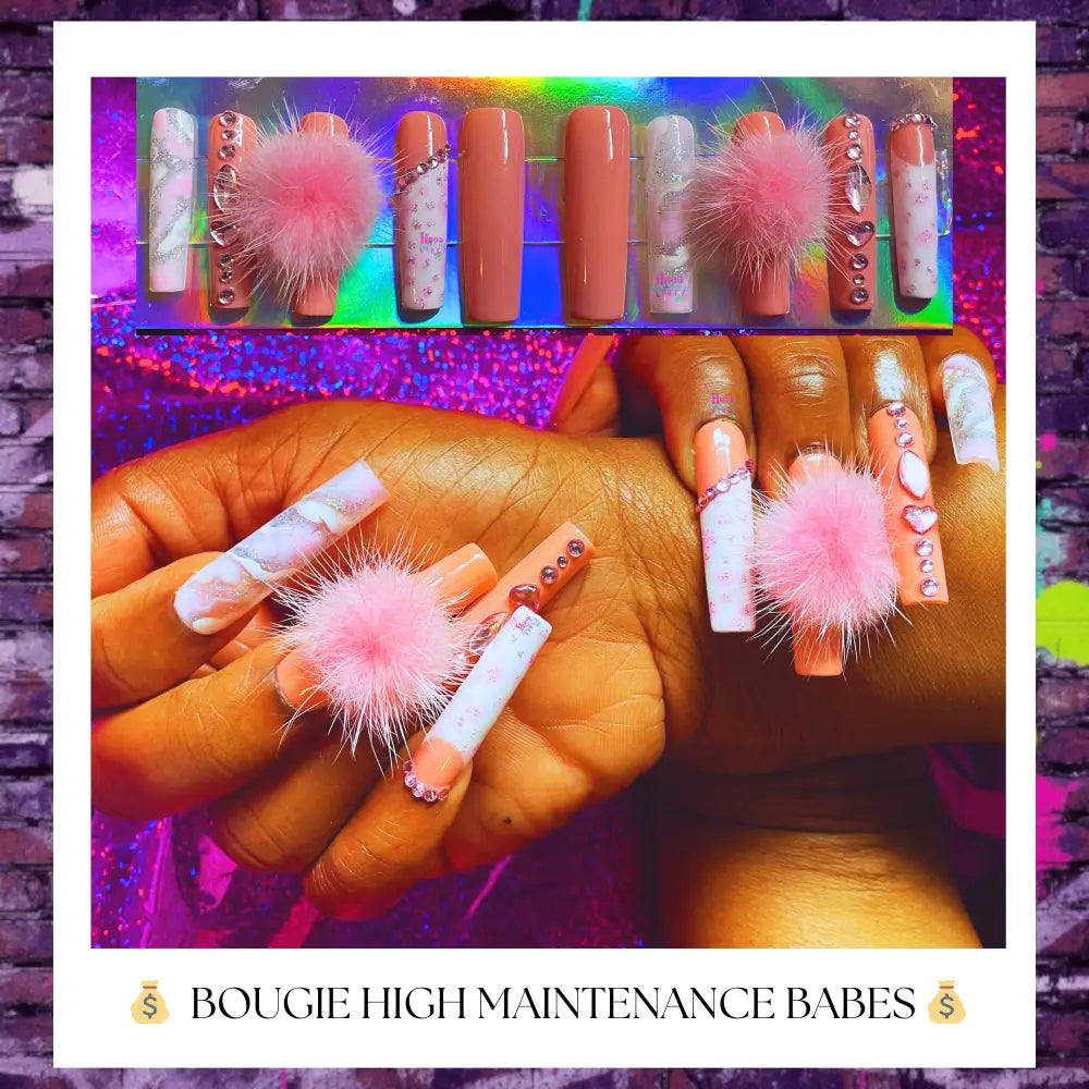 "A set of long square-shaped press-on nails in soft peach pink and white shades, decorated with rhinestones, marbled accents, and fluffy pink charms, displayed on medium brown hands against a pink feather background."
