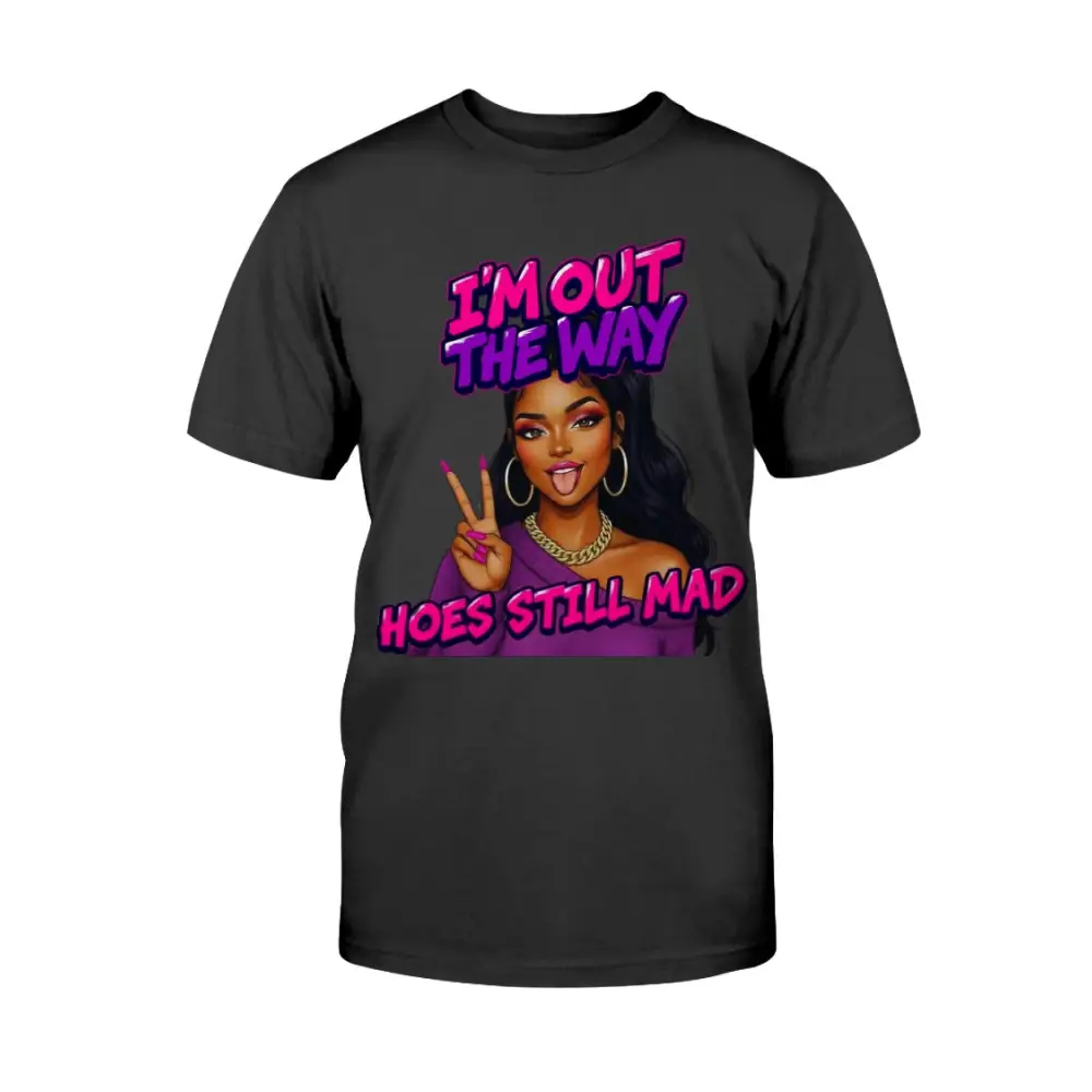 A black t-shirt featuring a cartoon-style Black woman with long hair, hoop earrings, gold chain, and pink nails flashing a peace sign, with bold pink and purple text that reads “I’m Out the Way, Hoes Still Mad.”"
