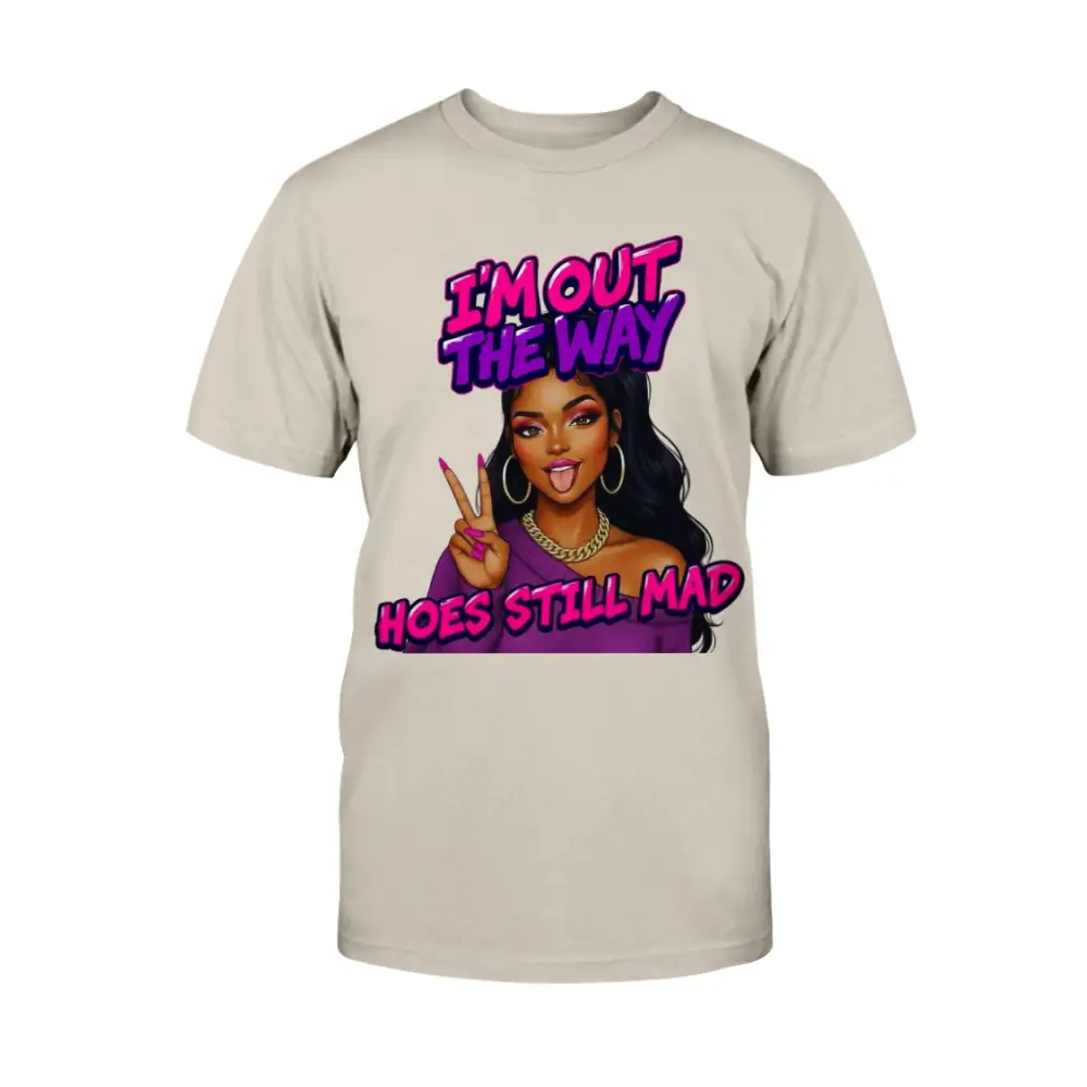 A beige t-shirt featuring a cartoon-style Black woman with long hair, hoop earrings, gold chain, and pink nails flashing a peace sign, with bold pink and purple text that reads “I’m Out the Way, Hoes Still Mad.”"